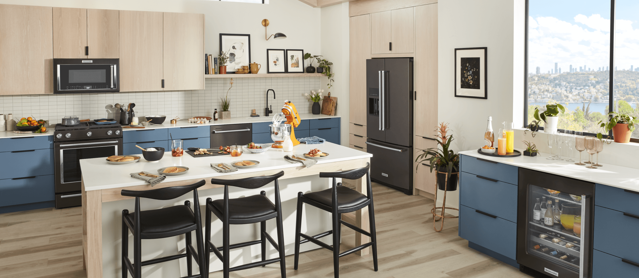 A contemporary kitchen with sleek blue cabinetry, black stainless steel appliances and a bright, honey colored KitchenAid® stand mixer.