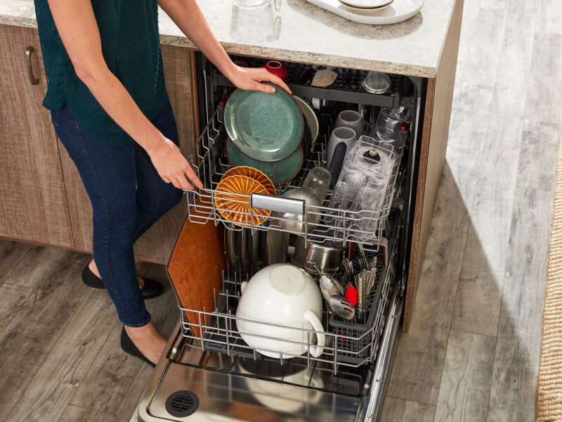 Person loading rustic green plates into a dishwasher