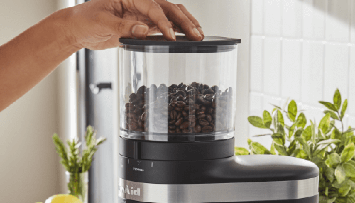 A woman preparing to process coffee beans in a black coffee grinder. 