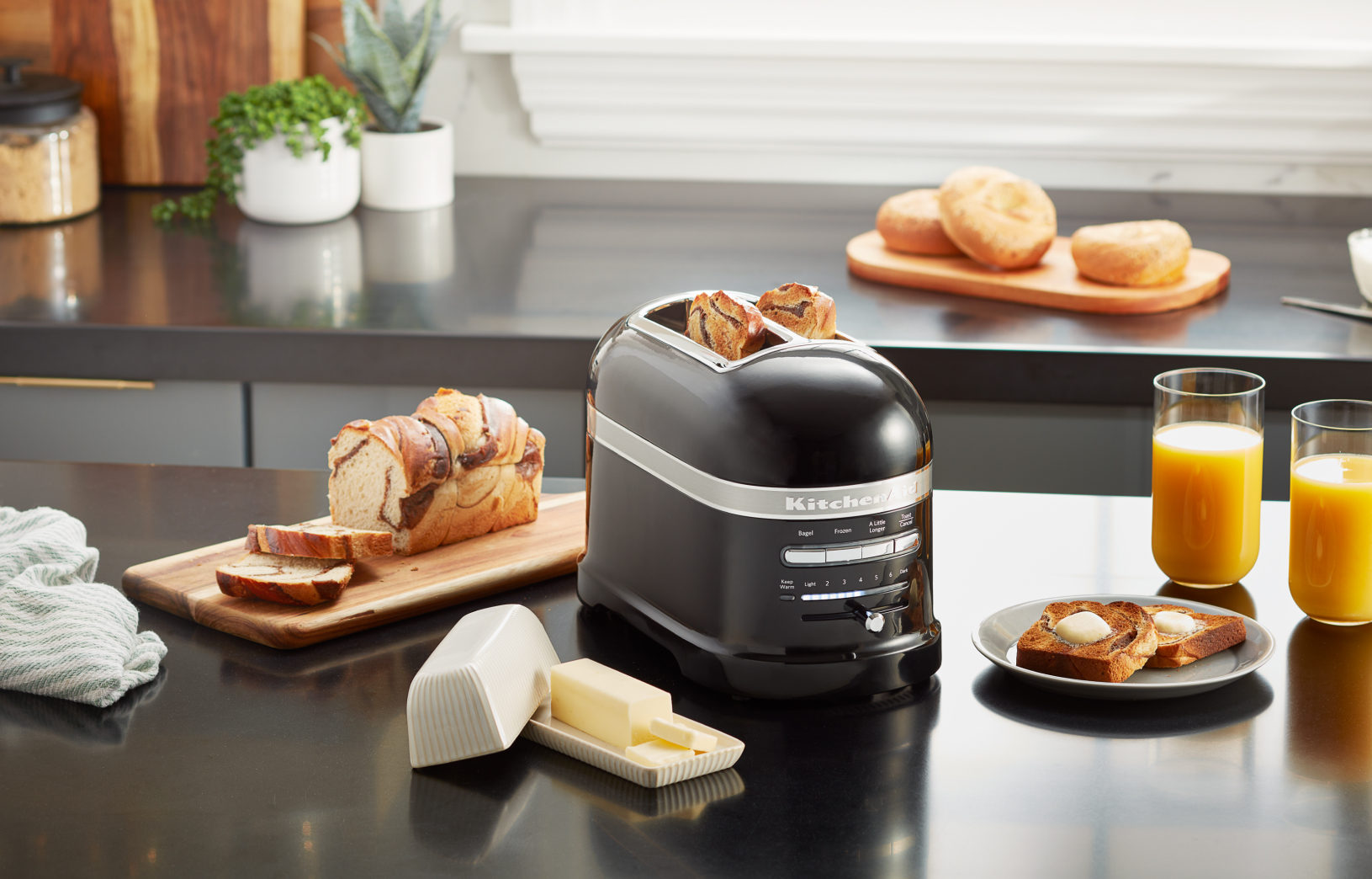 A KitchenAid® Pro Line® toaster surrounded by various breads, butter and glasses of orange juice.