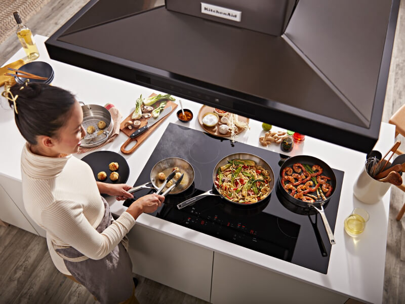 Bird's-eye view of person frying food on an electric stovetop beneath a range hood