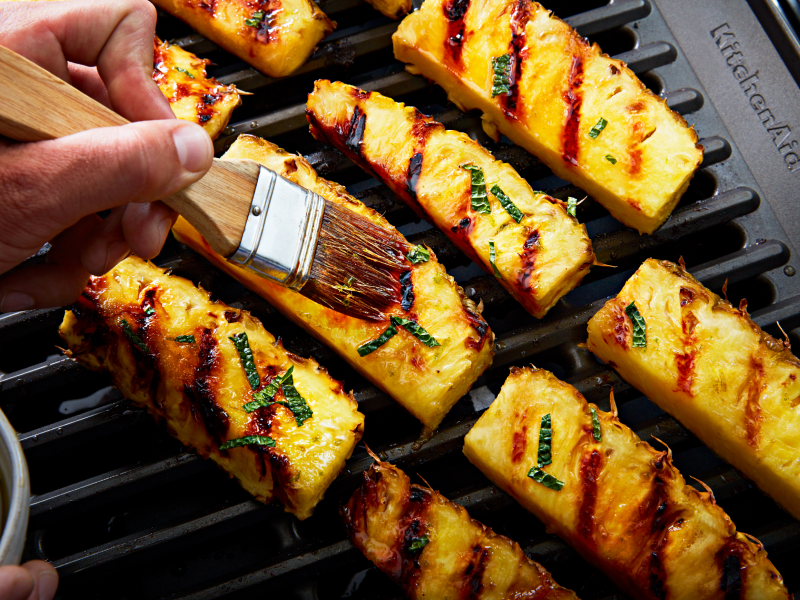 Hand dressing grilled pineapples with a pastry brush
