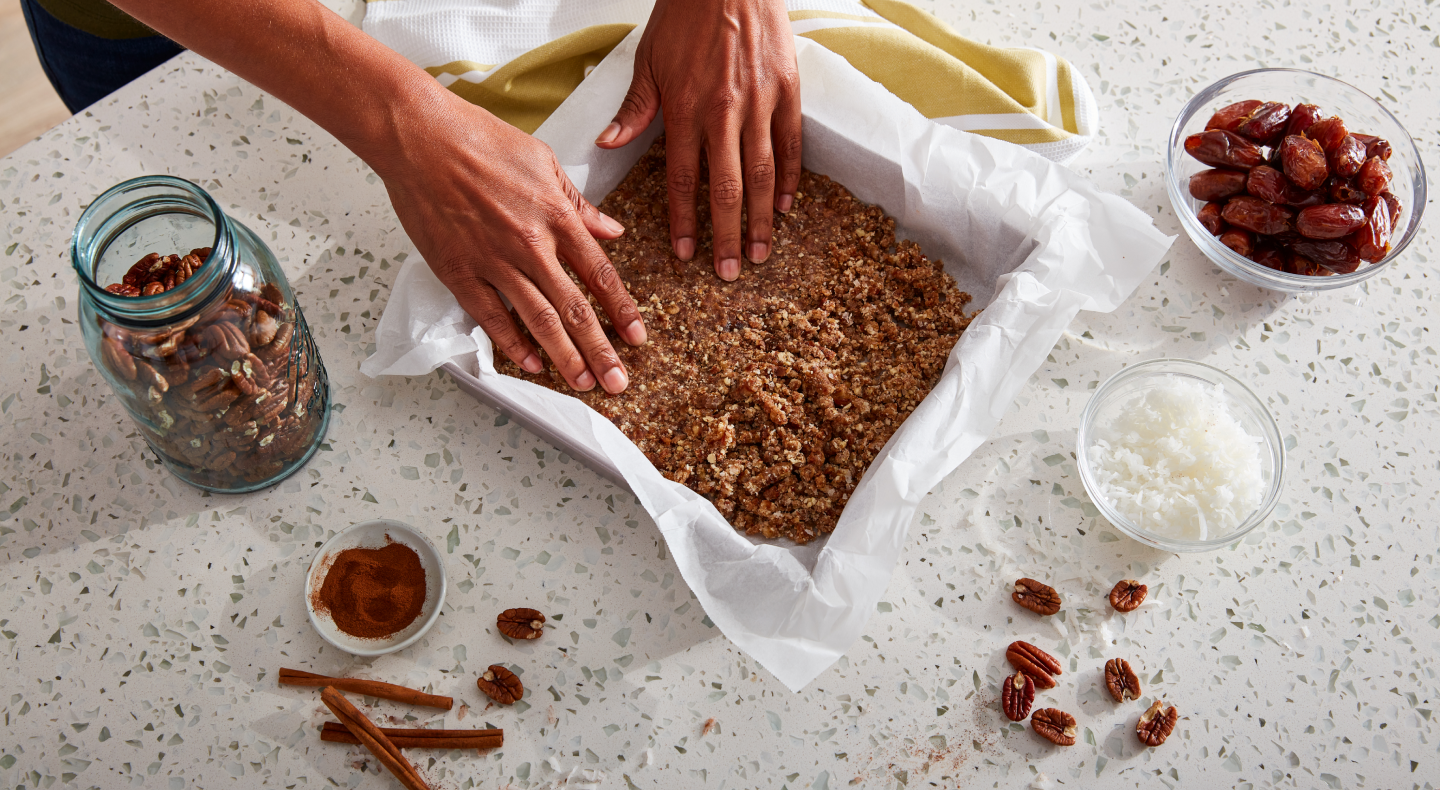A pair of hands putting a baking dish together with ingredients consisting of coconut, dates, pecans and cinnamon