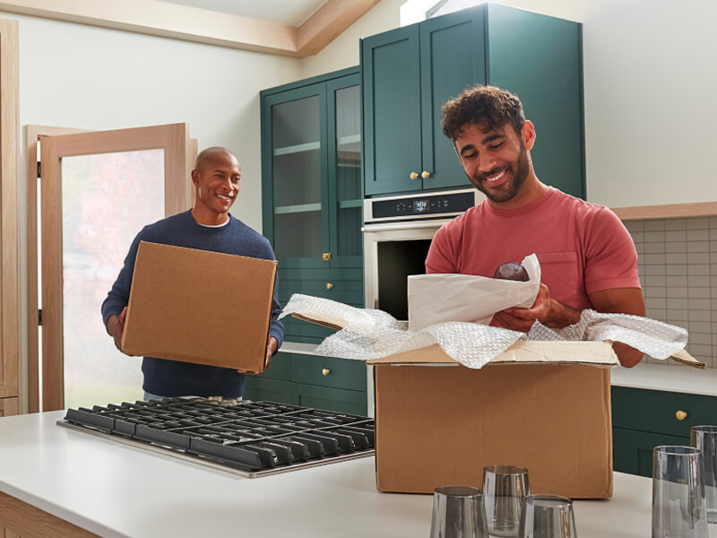 Two men moving and unpacking boxes in a remodeled kitchen