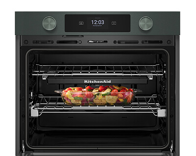 Open oven door with vegetables in a casserole dish inside