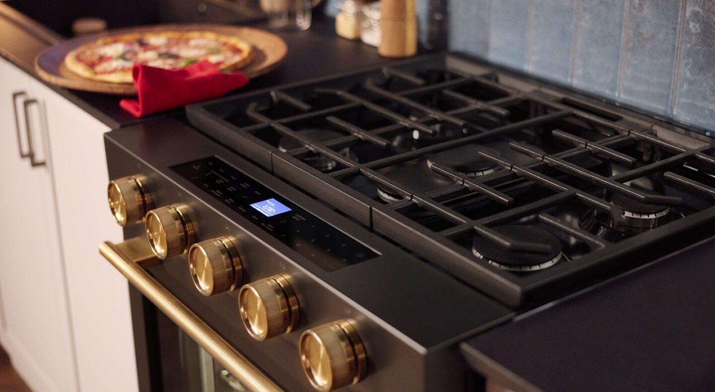 Close-up of gas stovetop burners next to cooked pizza on the countertop