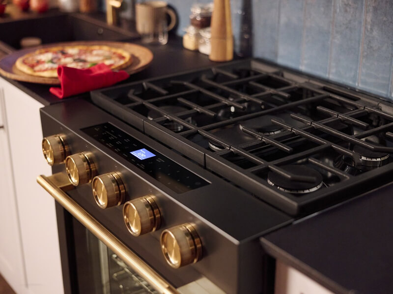 Close-up of gas stovetop burners next to cooked pizza on the countertop