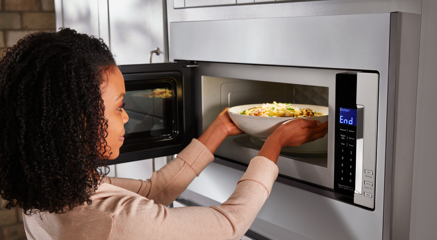 A person placing a dish in an open KitchenAid® microwave