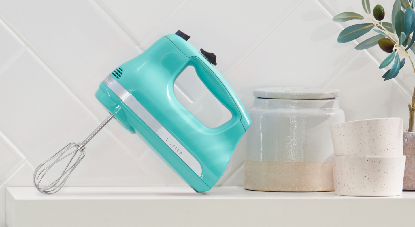 A teal KitchenAid® hand mixer on a modern kitchen counter.