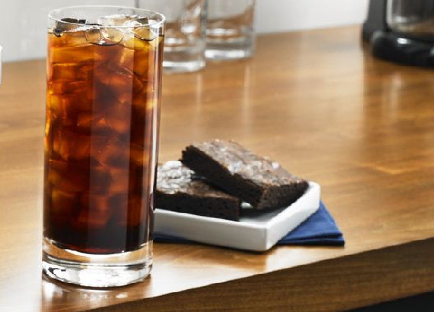 Tall glass of black iced coffee next to two brownies