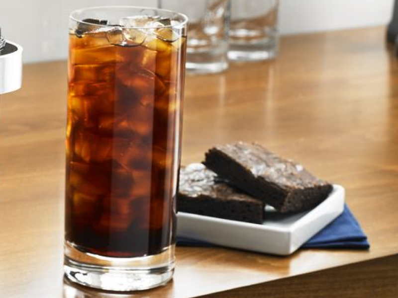 Tall glass of black iced coffee next to two brownies