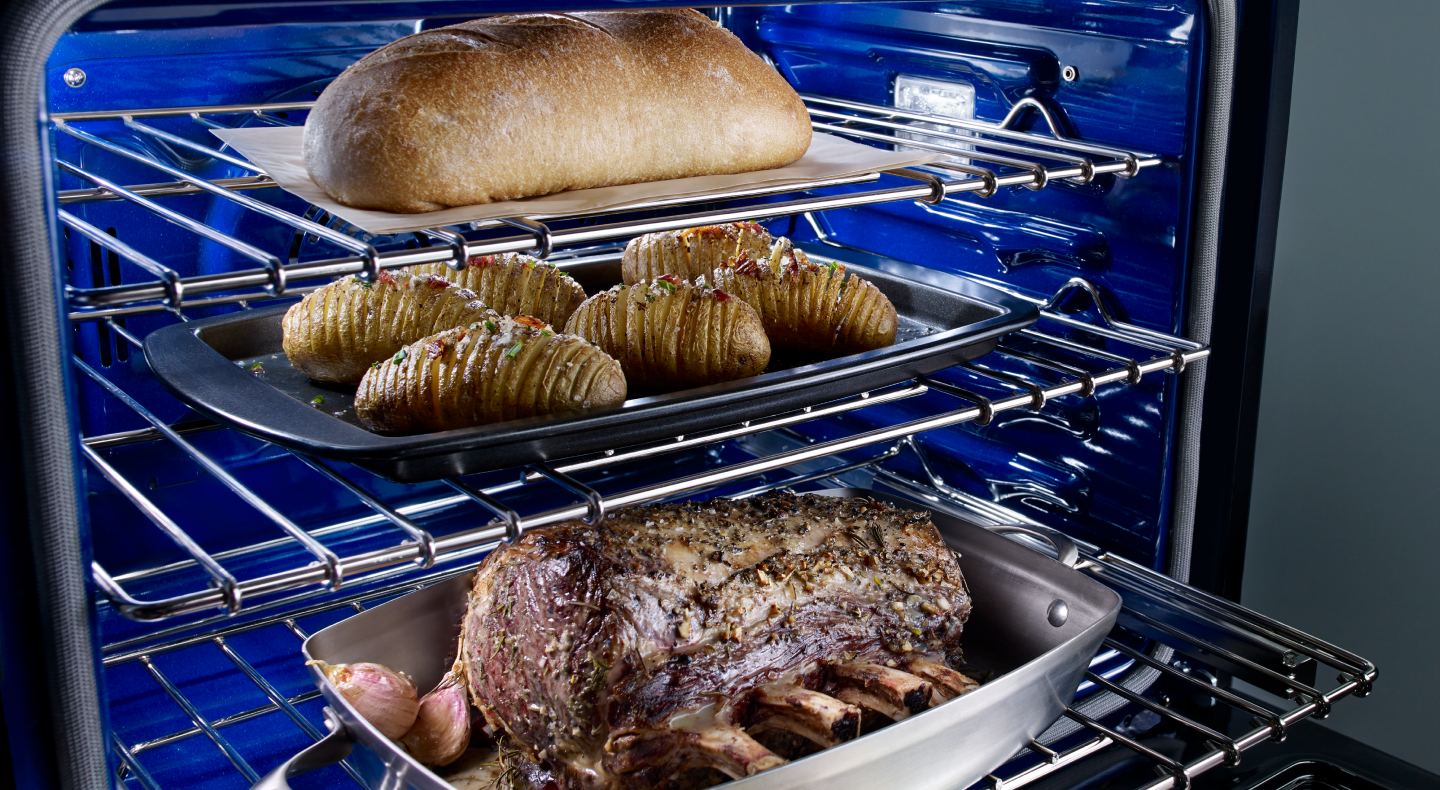 A rack with trays of meat, potatoes and a loaf of bread