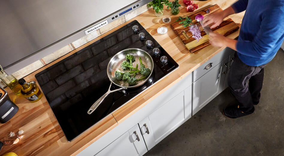 Broccoli resting in a pan and vegetables being sliced on a cutting board