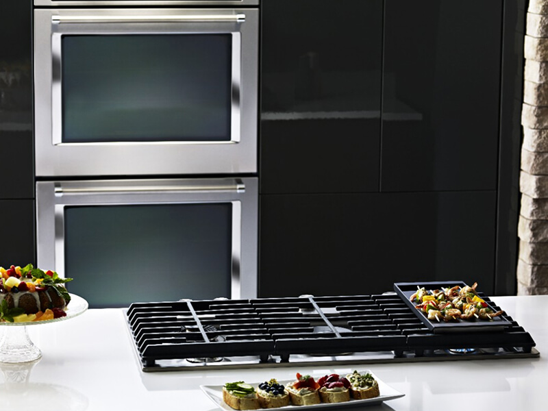 A KitchenAid® gas cooktop with a double KitchenAid® wall oven in the background