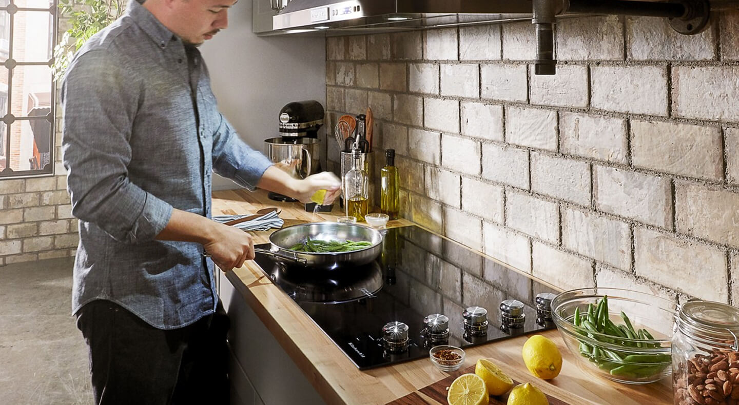 A person cooking on a KitchenAid® electric cooktop