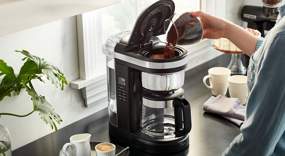 Person pouring coffee grounds into a KitchenAid® 12-Cup Coffee Maker