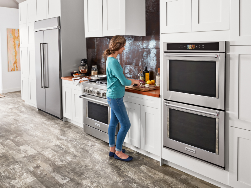 A woman chopping vegetables next to a KitchenAid® double wall oven