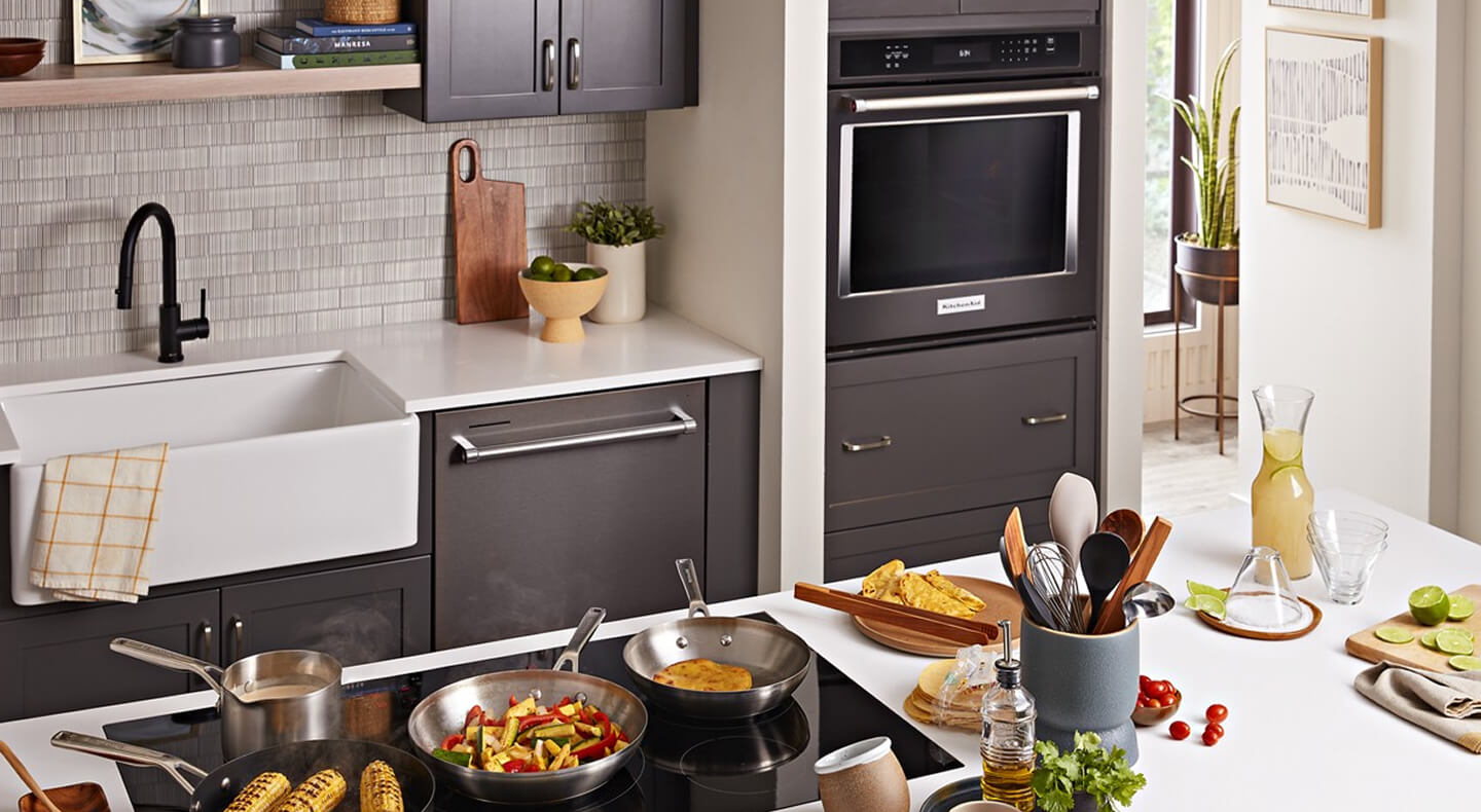 A galley kitchen with dark brown cabinetry, white countertops, a sink and built-in oven on one side, and an island with white countertops and a stovetop on the other