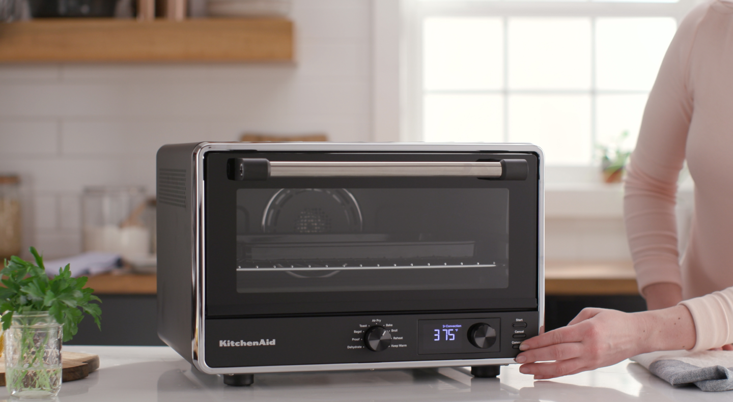 Person setting controls on a KitchenAid® countertop oven