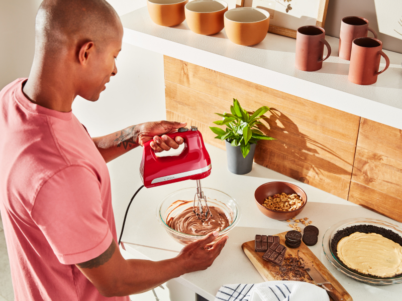 A man using a KitchenAid® hand mixer to make chocolate pie filling.