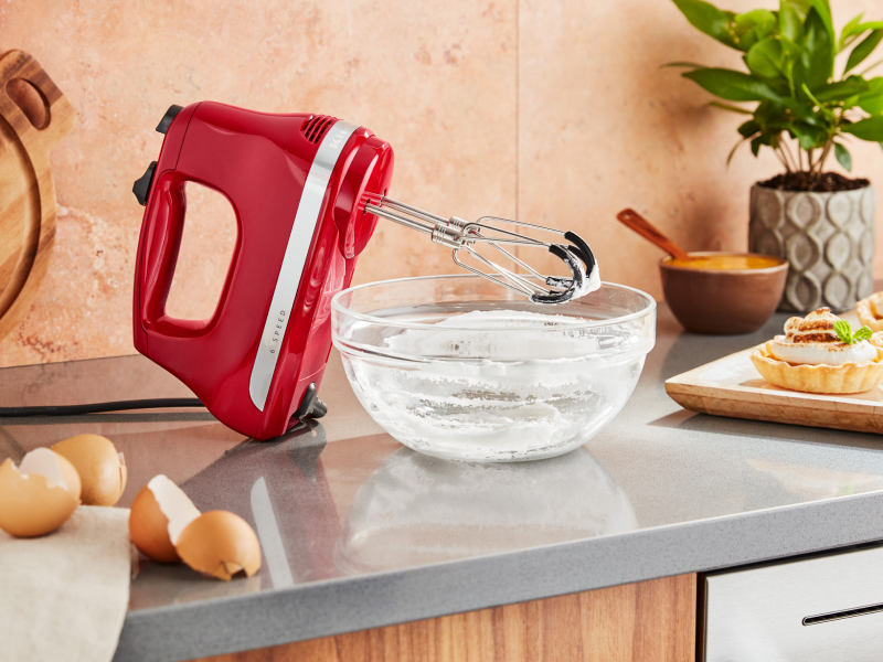 KitchenAid® hand mixer next to an empty mixing bowl of whipped egg whites and meringue tarts.