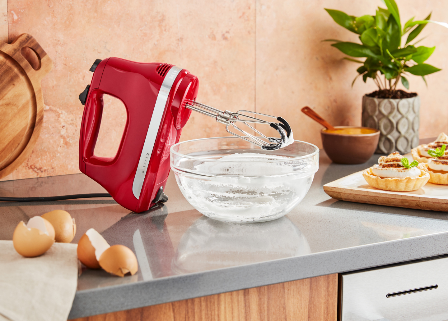 KitchenAid® hand mixer next to an empty mixing bowl of whipped egg whites and meringue tarts.