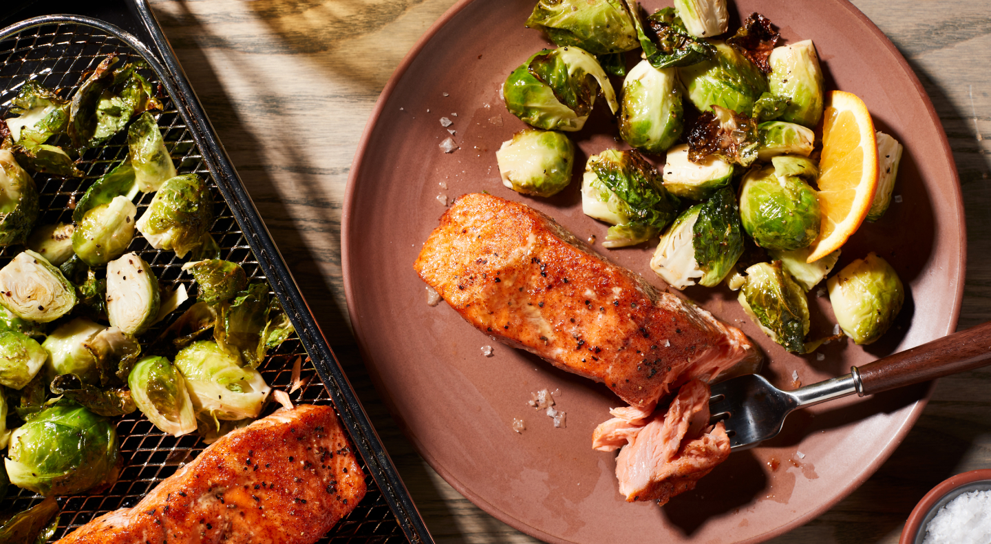 Air fryer salmon and Brussel sprouts on a plate next to an air fry basket with salmon and Brussel sprouts.