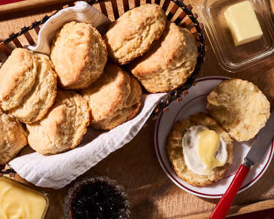Basket of biscuits next to prepared biscuit on plate with butter knife