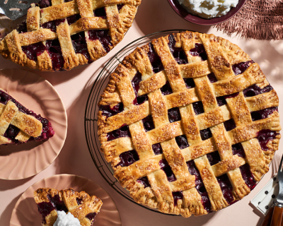 Whole blueberry lattice pie surrounded by plates with slices of blueberry pie