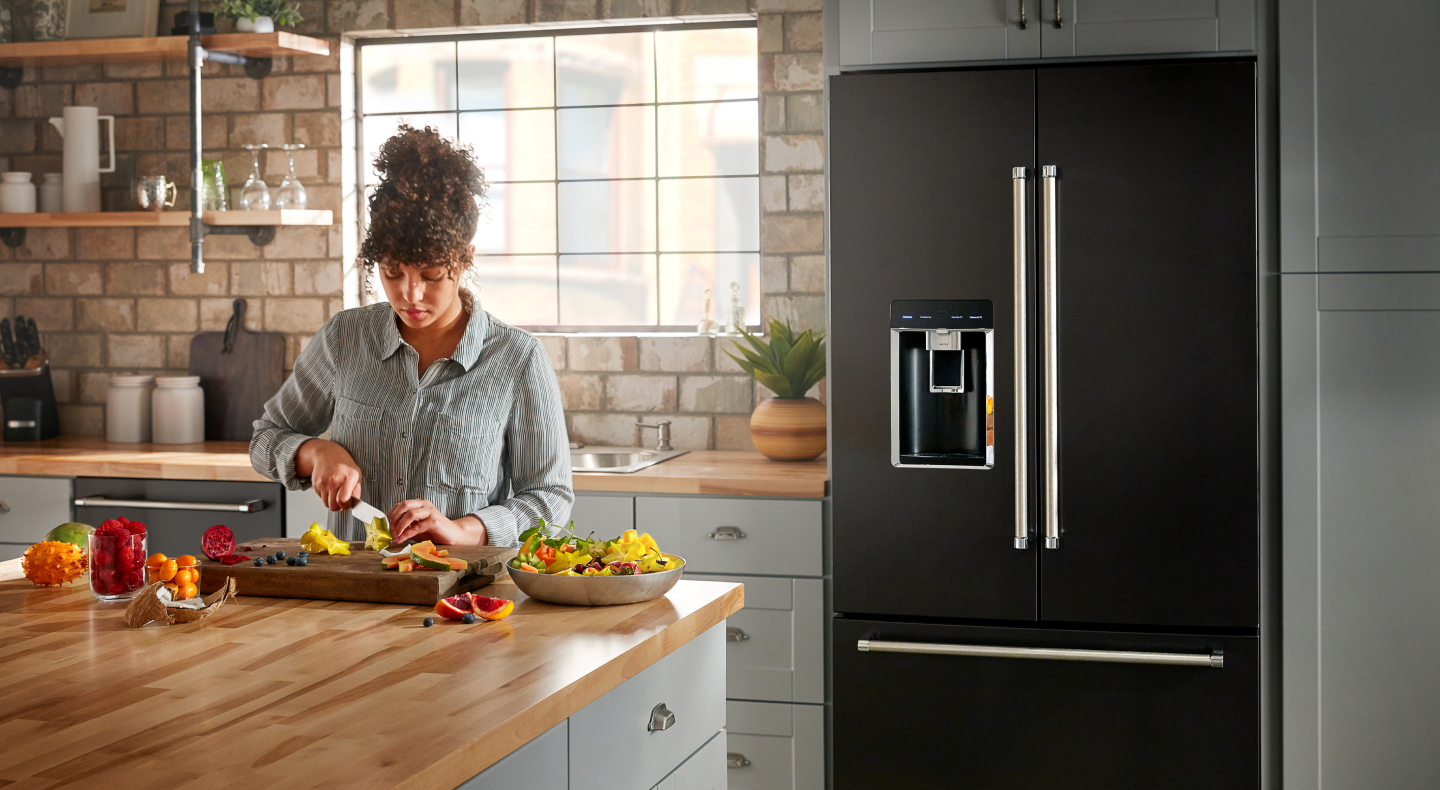 A person making a meal in a modern kitchen next to a KitchenAid® refrigerator.