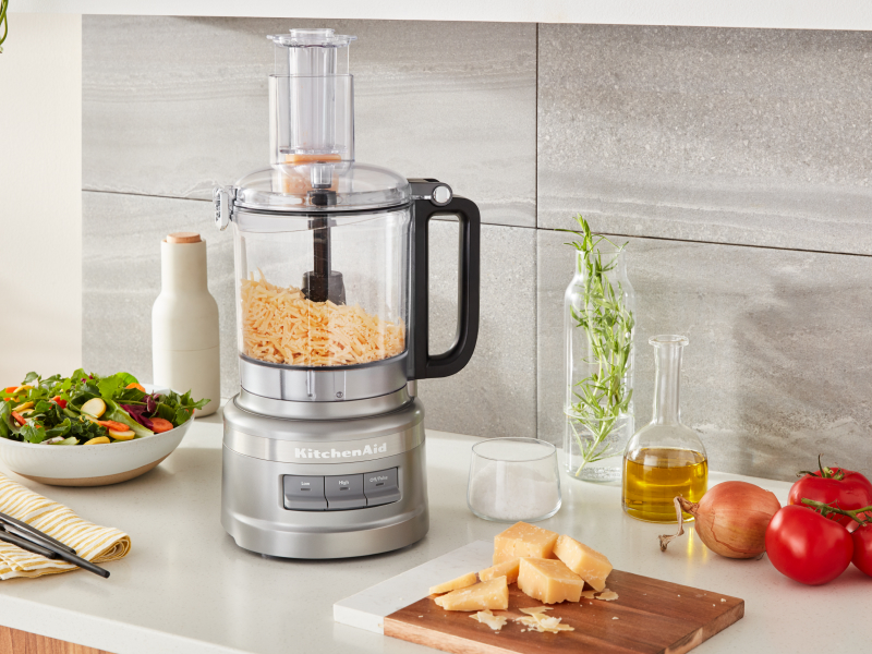 Shredded cheese in a food processor next to a salad