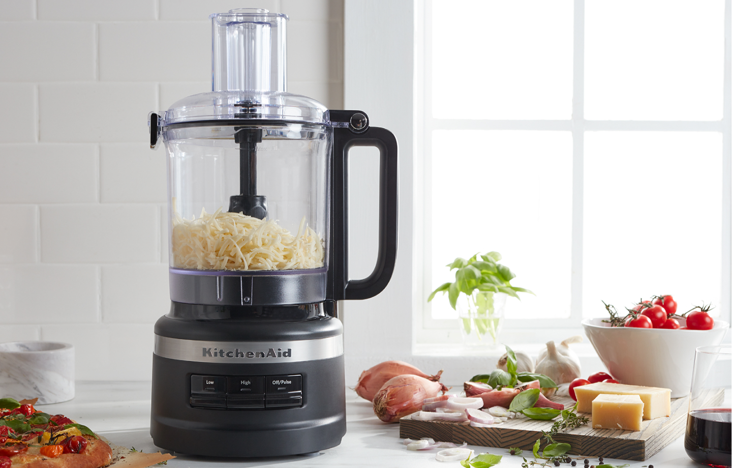Shredded cheese in a food processor next to a pizza