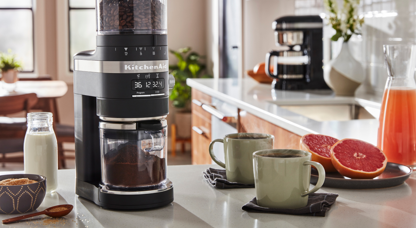 Coffee maker on counter with mugs full of coffee and halved grapefruit pieces 