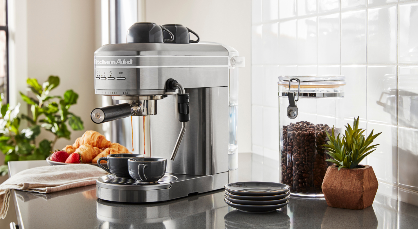 Silver KitchenAid® Semi-Automatic Espresso Machine on counter with coffee beans and croissants