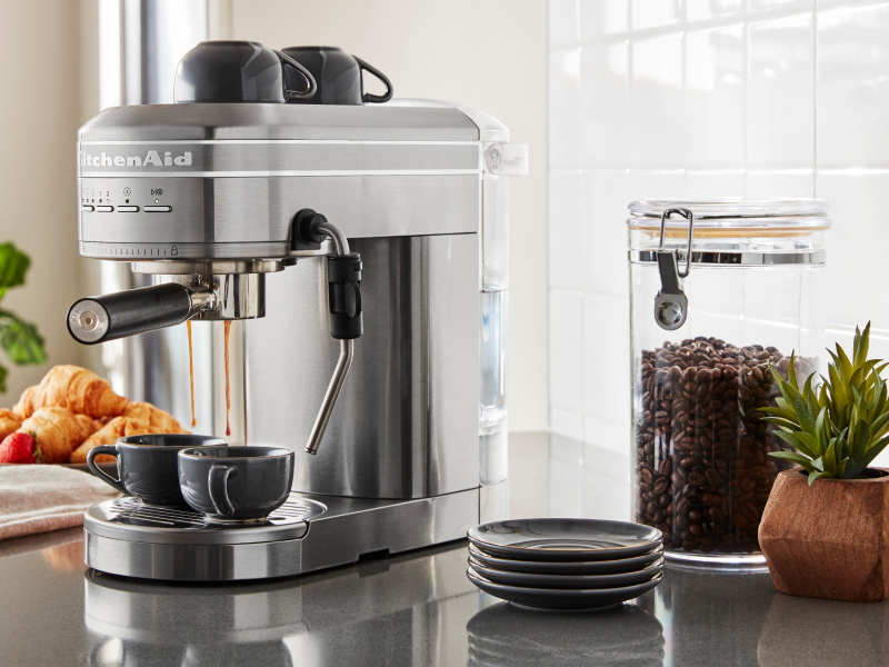 Silver KitchenAid® Semi-Automatic Espresso Machine on counter with coffee beans and croissants