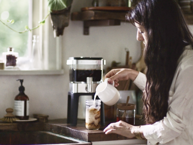 Person pouring milk into cup of cold brew coffee