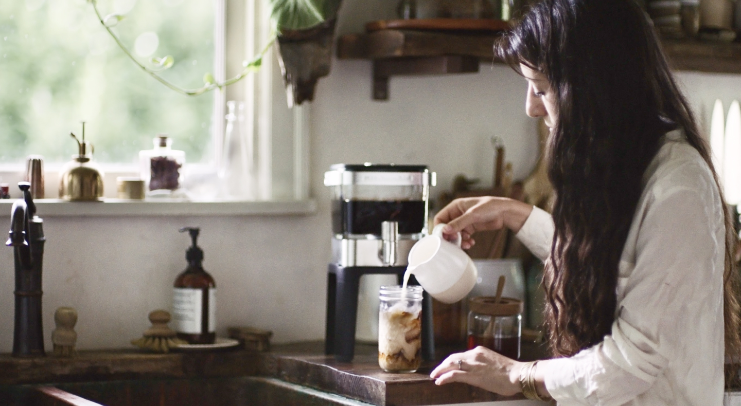 Person pouring milk into cup of cold brew coffee