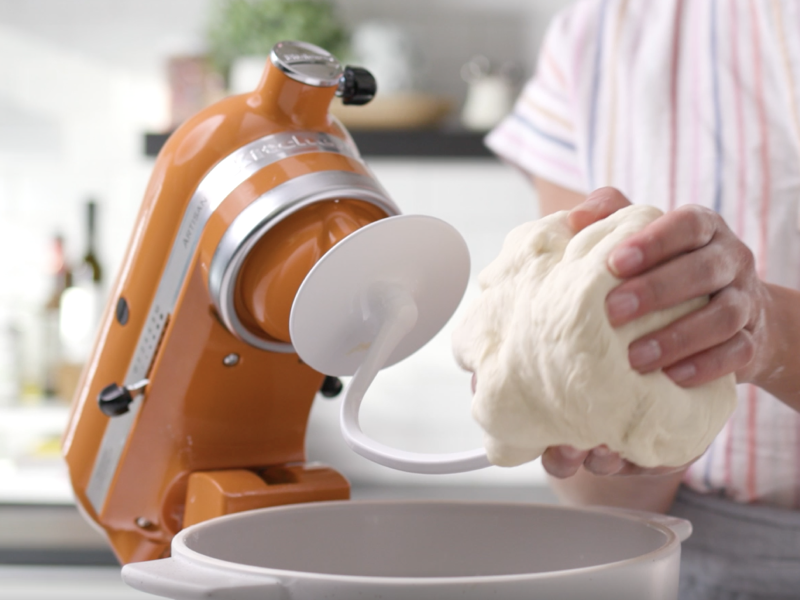 Bread dough being removed from a dough hook attached to an orange tilt-head KitchenAid® stand mixer.