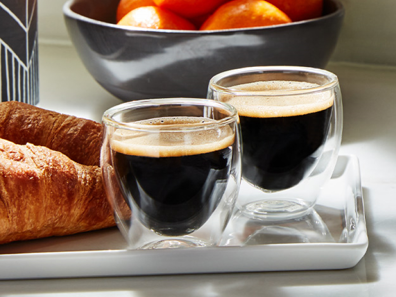 Two red eye espresso beverages on dish with croissants 