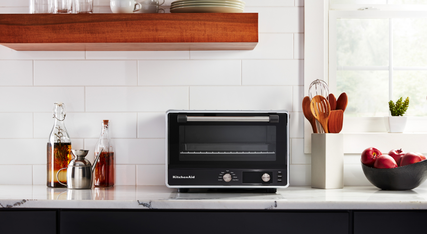 A KitchenAid® countertop oven with marinades and apples nearby.