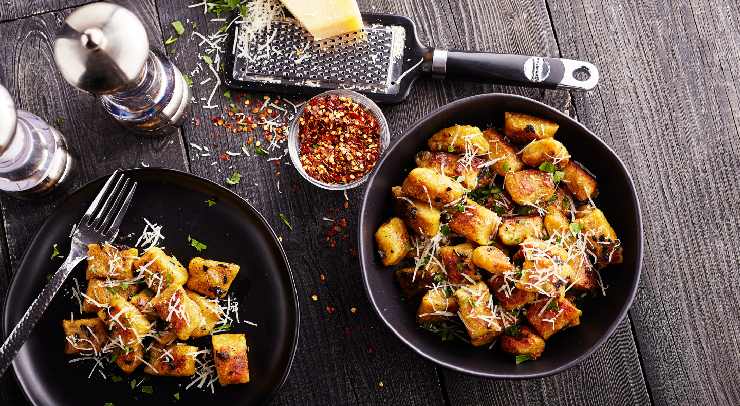 Two bowls of potato gnocchi meals with fresh parmesan, red pepper flakes and herbs. 