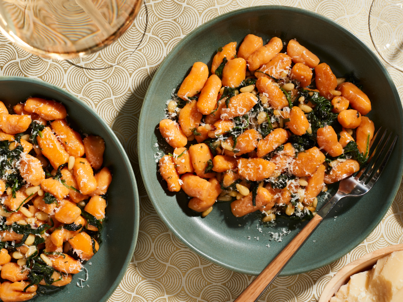 Two bowls of sweet potato gnocchi meals with shaved parmesan, spinach and herbs.