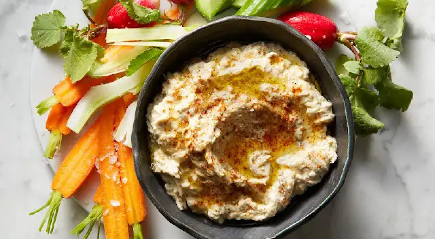 Baba ganoush in black bowl surrounded by freshly chopped carrots and radishes
