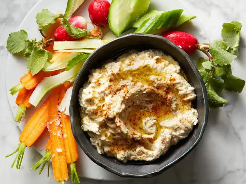 Baba ganoush in black bowl surrounded by freshly chopped carrots and radishes