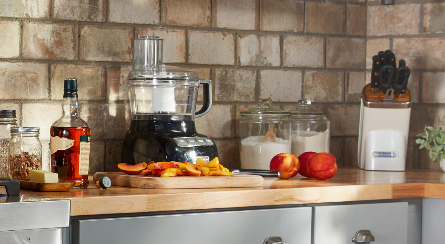 Sliced peaches on counter with ingredients and food processor