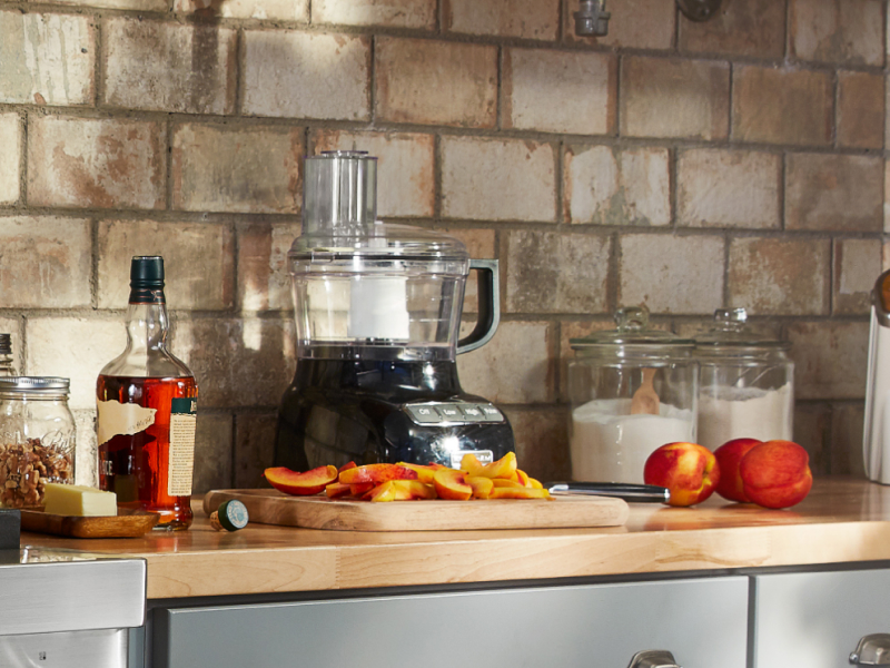 Sliced peaches on counter with ingredients and food processor