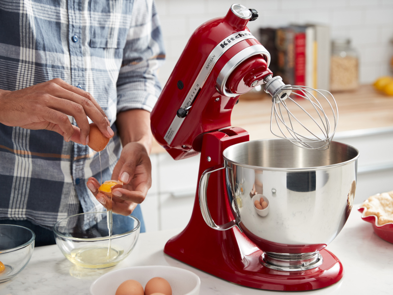 Person cracking eggs next to a KitchenAid® stand mixer with wire whip
