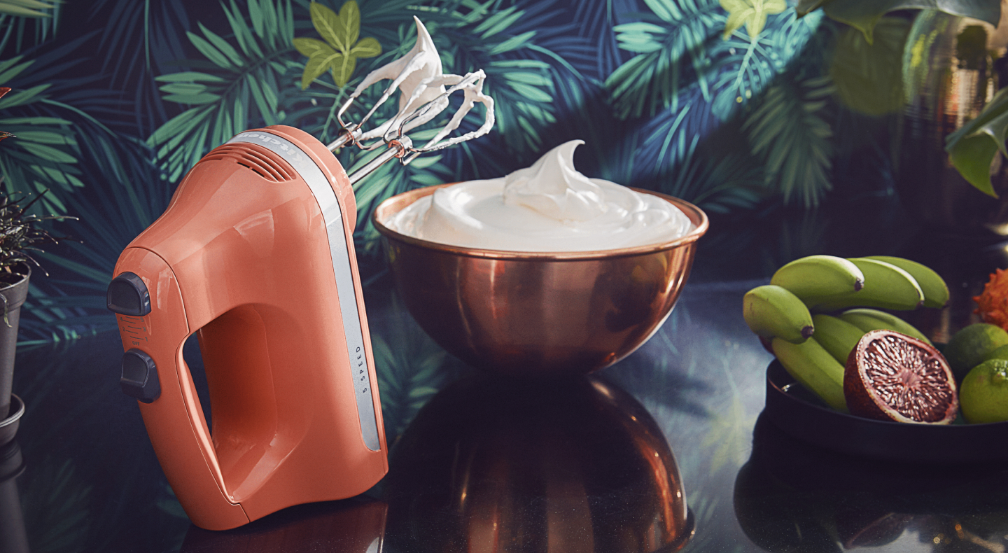 Orange KitchenAid® hand mixer next to a bowl of whipped cream