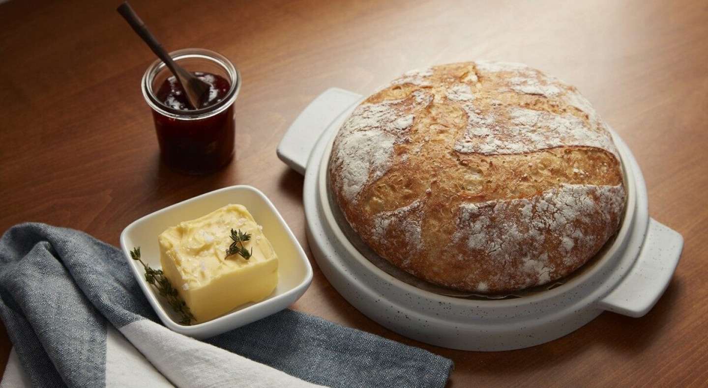 Round sourdough loaf next to a garnished butter dish and jar of jam spread