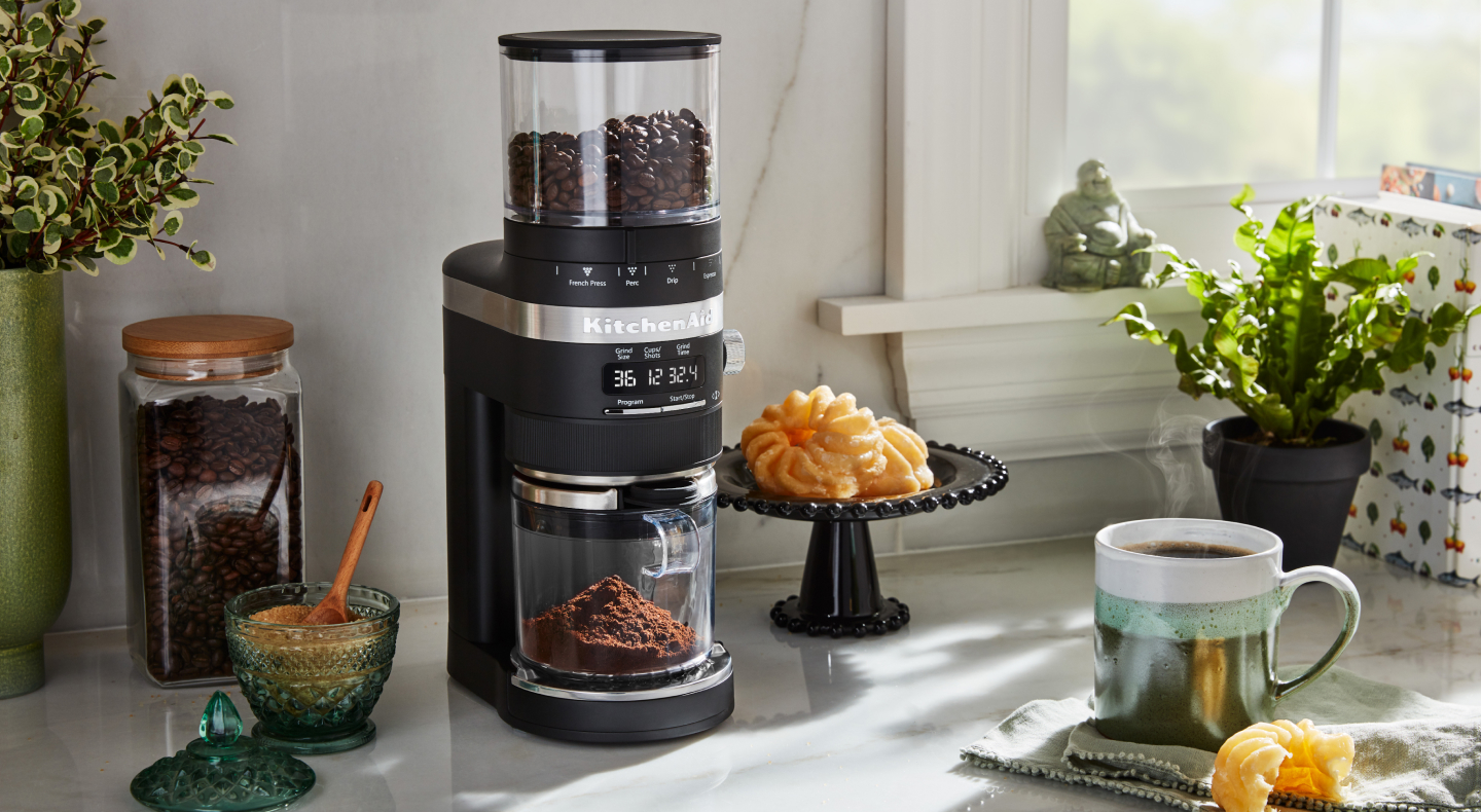 Burr grinder on a counter with pastries and brewed coffee